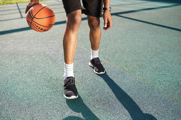 Muscular legs of unrecognizable basketball player training in outdoor court, copy space