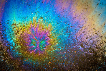 Colored oil stain on the asphalt. A rainbow slick of gasoline. Abstract background.