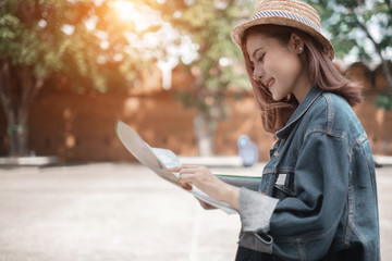 Smiling woman traveler in thapae gate landmark chiangmai thailand with backpack holding world map on holiday, relaxation concept, travel concept