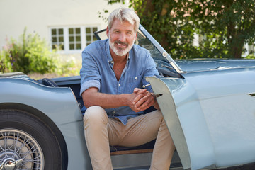 Portrait Of Proud Mature Man Sitting In Restored Classic Sports Car Outdoors At Home - Powered by Adobe