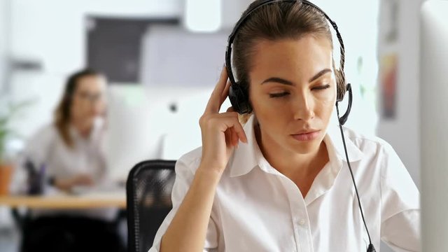 Young serious business woman working in office using pc computer and headphones with mic talking