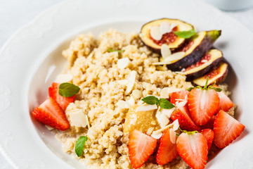 Quinoa breakfast porridge with strawberries and figs in white plate. Healthy breakfast concept.