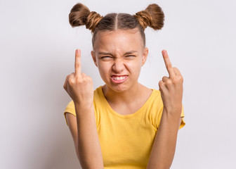 Portrait of angry teen girl showing middle finger, on gray background. Beautiful caucasian young teenager making grimace and obscene gesture. Cute child shows bad sign and looking at camera.