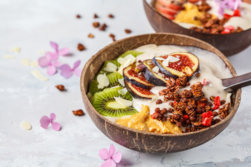 Smoothie bowl with fruit and granola with coconut shell bowl on gray background. Healthy vegan food concept.