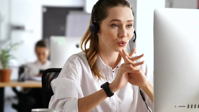 Young beautiful happy business woman working in office using pc computer and headphones with mic