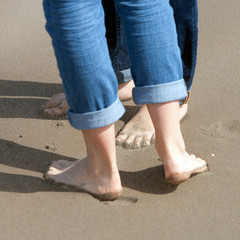 two pairs of feet close together on sand of beach