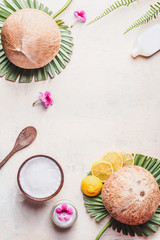Coconut oil in wooden bowl with spoon and moisturizing cream on white desk background with tropical leaves and flowers , top view. Frame. Copy space. Flat lay. Modern skin care and cosmetic concept