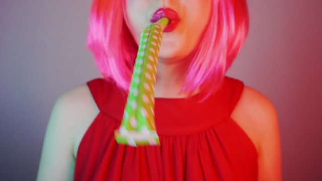 Woman in a bright pink wig at a party. She is blowing at a party horn. Birthday Celebration.