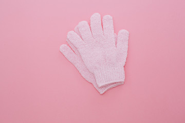 Woman exfoliating massage glove for shower on pink background.Gloves for use in the shower for massage and scrub. Beauty background with cosmetic products. Beauty, health and spa concept