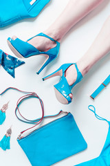 Woman legs in sexy turquoise bright pumps lie on white floor background with fashion outfit accessories: handbag, belt, churches, jacket,silk top. Top view. Flat lay. Creative layout.