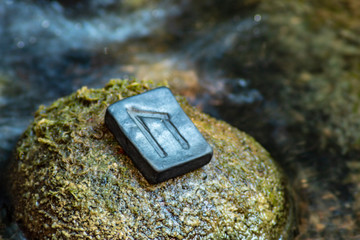 Norse rune Uruz on the stone and the evening river background. Health, strength, masculinity. The energy of the earth.