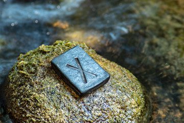 Norse rune Gebo (Gibu) on the stone and the evening river background. Gift, balance, harmony, giftedness. The rune is associated with the supreme Scandinavian God Odin.