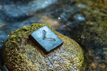 Norse rune Kennaz on the stone and the evening river background. Knowledge, decision, way out of a difficult situation. Helps to work with any data and information.