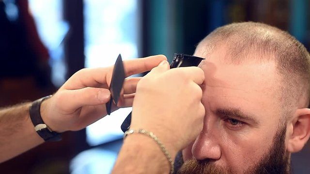 Barber hands doing combing and cutting for aligning length and shaping of forelock of hair on male head with cropped view. Using comb and electric trimmer clipper machine in modern hairdressing salon