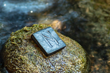 Norse rune Hagalaz (Hagal) on the stone and the evening river background. Excitement, shake, exit the comfort zone. Getting rid of old unnecessary patterns.