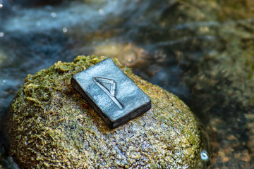 Norse rune Vunjo on the stone and the evening river background. Joy, luck, fulfillment of desires.