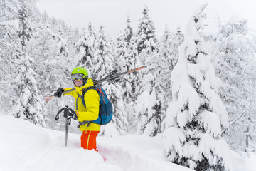 Fototapeta na wymiar Man in yellow with blue backpack skiing stay with many firs around and soft powdery snow. The backcountry skier is on Alps Mountain in Austria.