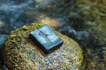 Norse rune Nautiz (Naud) on the stone and the evening river background.  Obstacles, the necessary awareness of difficulties and opportunities to overcome them. Strong bond, obligations.