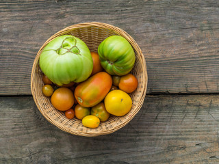 Obraz na płótnie Canvas Various green, yellow, red, large, small, ugly garden tomatoes in a wicker basket on a wooden background. Flat lay
