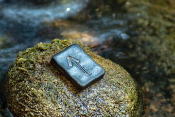 Norse rune Teihwaz (Tihwaz,Tyr) on the stone and the evening river background. Law, order, protection, nobility, courage. The rune is associated with the Scandinavian god Tür.