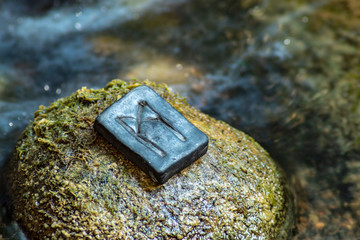 Norse rune Mannaz on the stone and the evening river background. Humanity, the development of the best human qualities. Self-realization. Work with human resources.