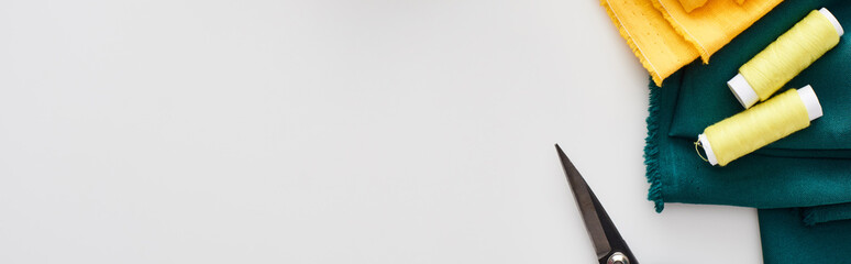 panoramic shot of fabric, scissors and threads on white background