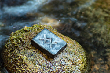 Norse rune Ingwaz on the stone and the evening river background. Seed, potential, energy, fertility. The rune is associated with the Scandinavian god Freyr.