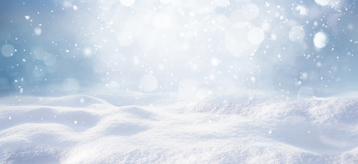 Winter snow background with snowdrifts, with beautiful light and snow flakes on the blue sky, beautiful bokeh circles, banner format, copy space.