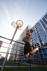 Low angle action shot of African basketball player jumping while shooting slam dunk in outdoor...