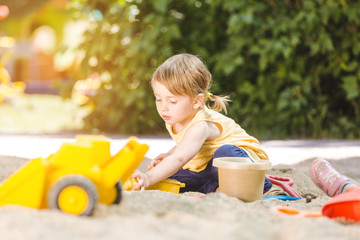 Little girl having lots of fun with her toys playing in the sandbox