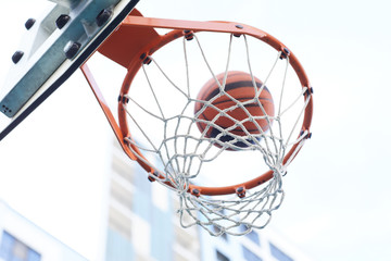 Fototapeta na wymiar Closeup of basketball shooting through hoop against urban background, copy space