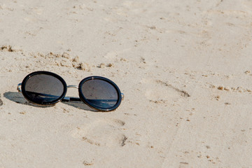Top view of sunglasses on the beach near the blue sea with sand