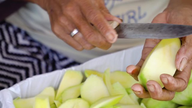 Female hands cut green mango into slices. Woman cuts a mango with a knife.