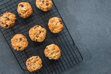 Homemade chocolate chip cookies with fruit and nuts cooling on a wire rack, dark background, flat lay, copy space