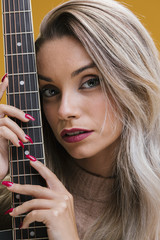 Attractive young woman holding guitar against yellow background