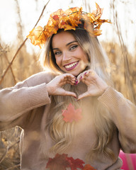 Attractive young woman wearing maple leaves tiara making heart shape with hand