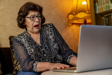 Senior woman use laptop. She looks very surprised. Surfing in a browser and social media. The woman...