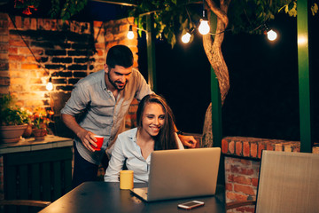 young couple using a laptop while relaxing at home together in backyard