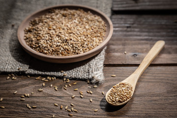 Flax seeds on wooden plate and wooden spoon, on wooden base.
