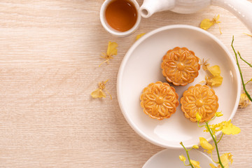 Obraz na płótnie Canvas Tasty moon cake for Mid-Autumn festival on bright wooden table, concept of festive afternoon tea decorated with yellow flowers, top view, flat lay.