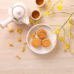 Tasty moon cake for Mid-Autumn festival on bright wooden table, concept of festive afternoon tea decorated with yellow flowers, top view, flat lay.