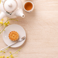 Tasty moon cake for Mid-Autumn festival on bright wooden table, concept of festive afternoon tea decorated with yellow flowers, top view, flat lay.