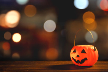 Halloween concept - Orange plastic pumpkin lantern on a dark wooden table with blurry sparkling light in the background, trick or treat, close up.