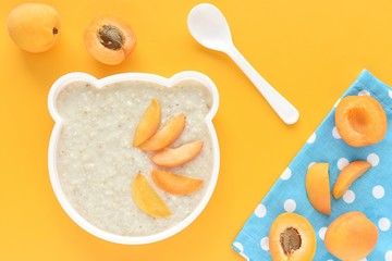 Healthy oatmeal and apricot porridge for kids in funny bear shape dish, top view on yellow background.