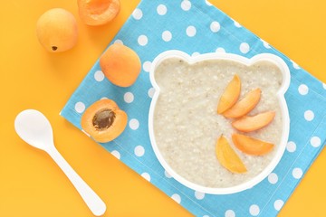 Healthy breakfast for kids, oatmeal porridge with apricot served in funny bear shape plate.