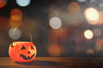 Halloween concept - Orange plastic pumpkin lantern on a dark wooden table with blurry sparkling...
