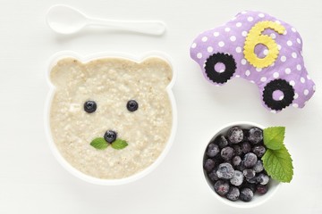 Start to eat oatmeal porridge from six month, funny plate in shape of bear, blueberries in bowl.