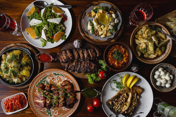 delicious dishes of Ukrainian and Georgian national cuisines placed on a large wooden table: meat, fish, adzhika, booze, salad, fried potatoes, cheese