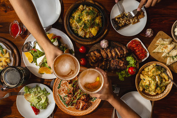 a large wooden table generously covered with delicious national dishes, with friends sitting and...