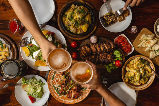 a large wooden table generously covered with delicious national dishes, with friends sitting and drinking light beer from glasses